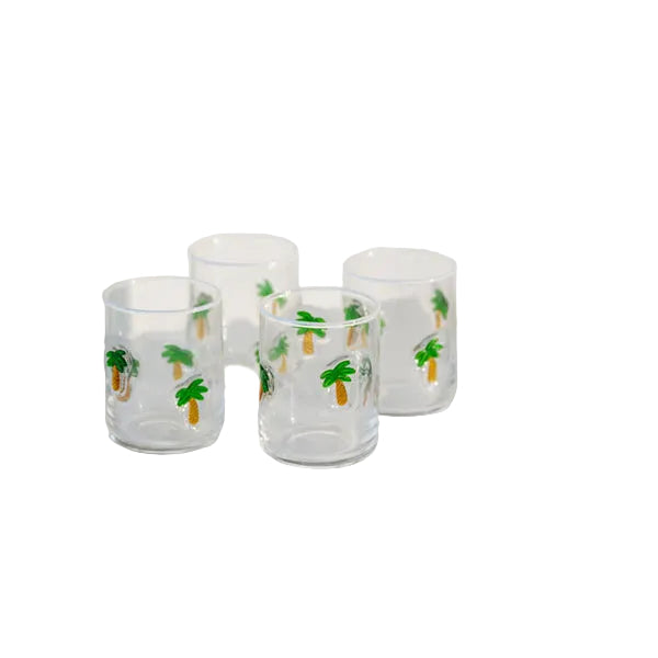 Set of four clear glass tumblers with a green palm tree print, on white