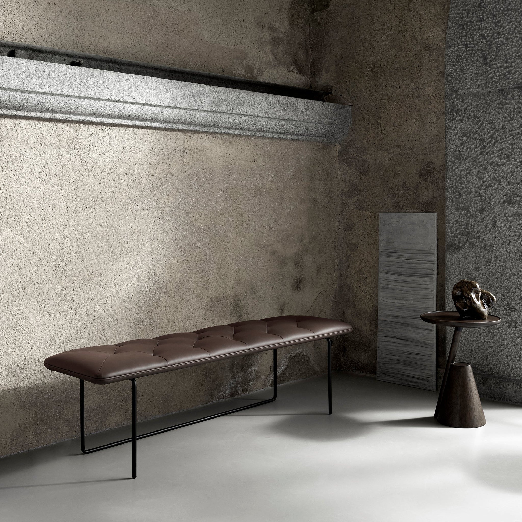 Modern brown bench in a minimalistic room with concrete walls and a small table.