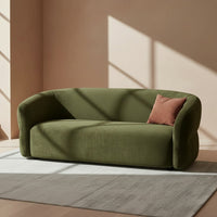Bauhaus Aura curved olive green fabric sofa with a wrap-around back and a small textured terracotta accent pillow.