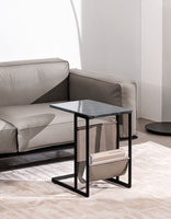 Cleo side table with a smoked glass top and a black frame beside a tan leather sofa