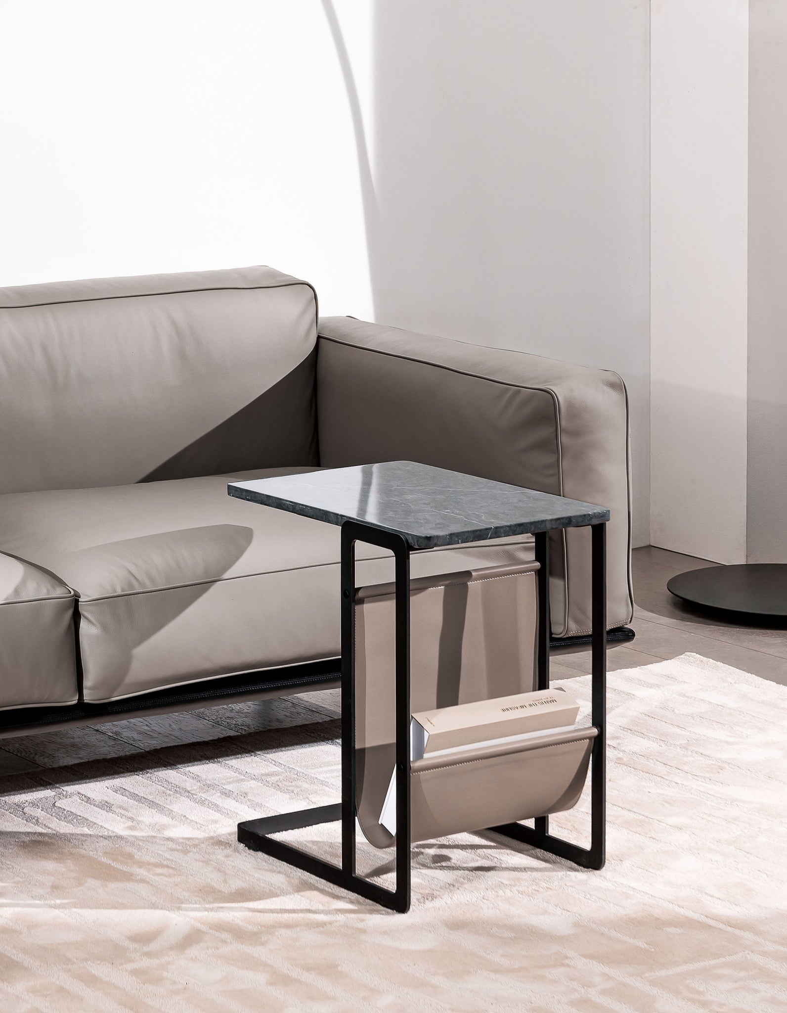 Cleo side table with a smoked glass top and a black frame beside a tan leather sofa