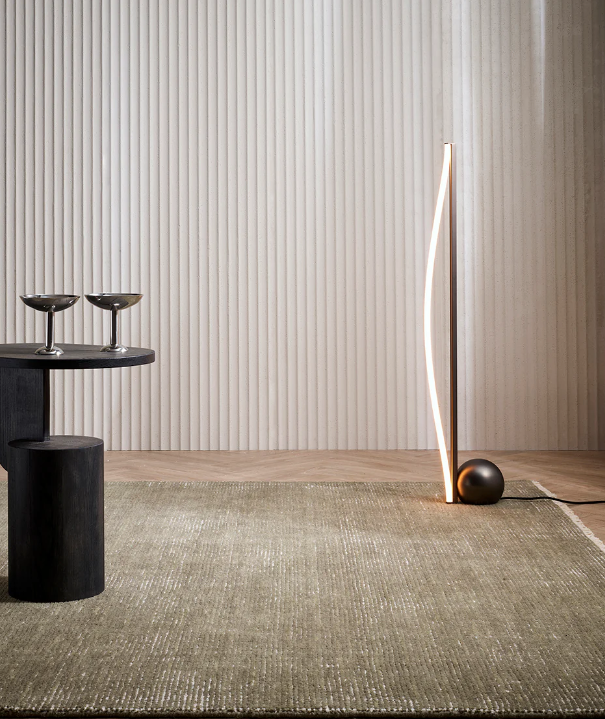 Corbett floor rug in sage green in a room with a slim floor lamp and a ribbed timber wall