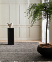 Corbett floor rug in charcoal beneath a black pedestal with a vase, beside a potted tree