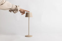 Hand touching the top of the Serene cordless table lamp in sand to switch it on
