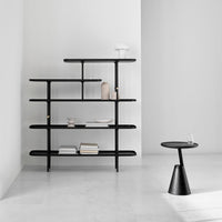 Mate side table in black beside a black open shelving unit in a bright white room